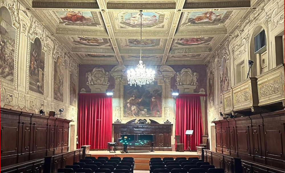 Sala principale del Circolo Lirico di Bologna che presenta un palco con un pianoforte. La sala è abbellita da affreschi alle pareti